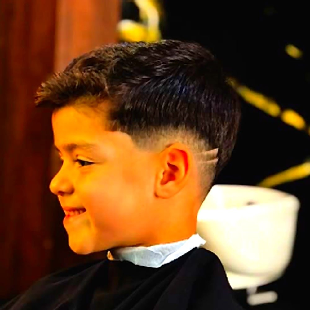 Criança sorrindo com corte degradê e desenho na lateral, feito na Santos Barber Studio, Resende - RJ