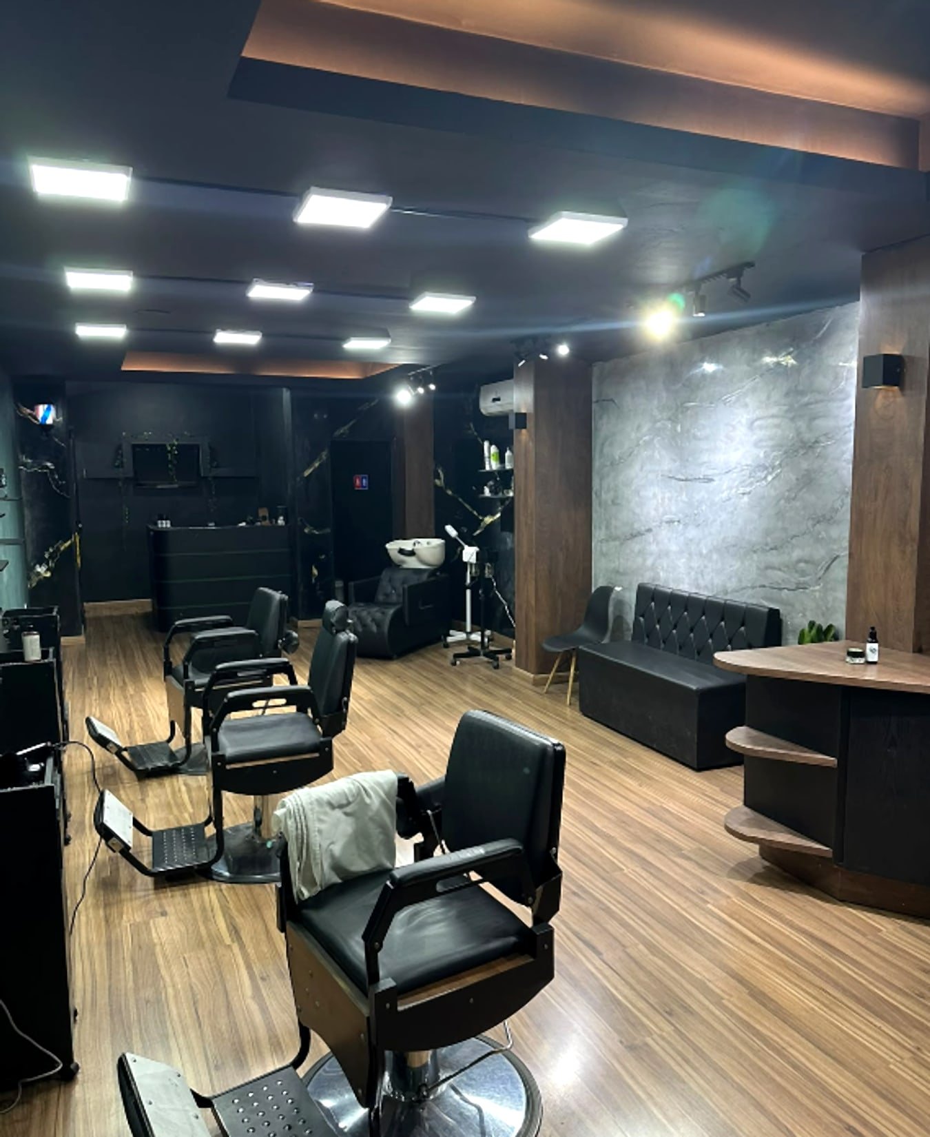 Interior climatizado da Santos Barber Studio, com cadeiras de barbeiro, sofá e balcão, em Campos Elíseos, Resende